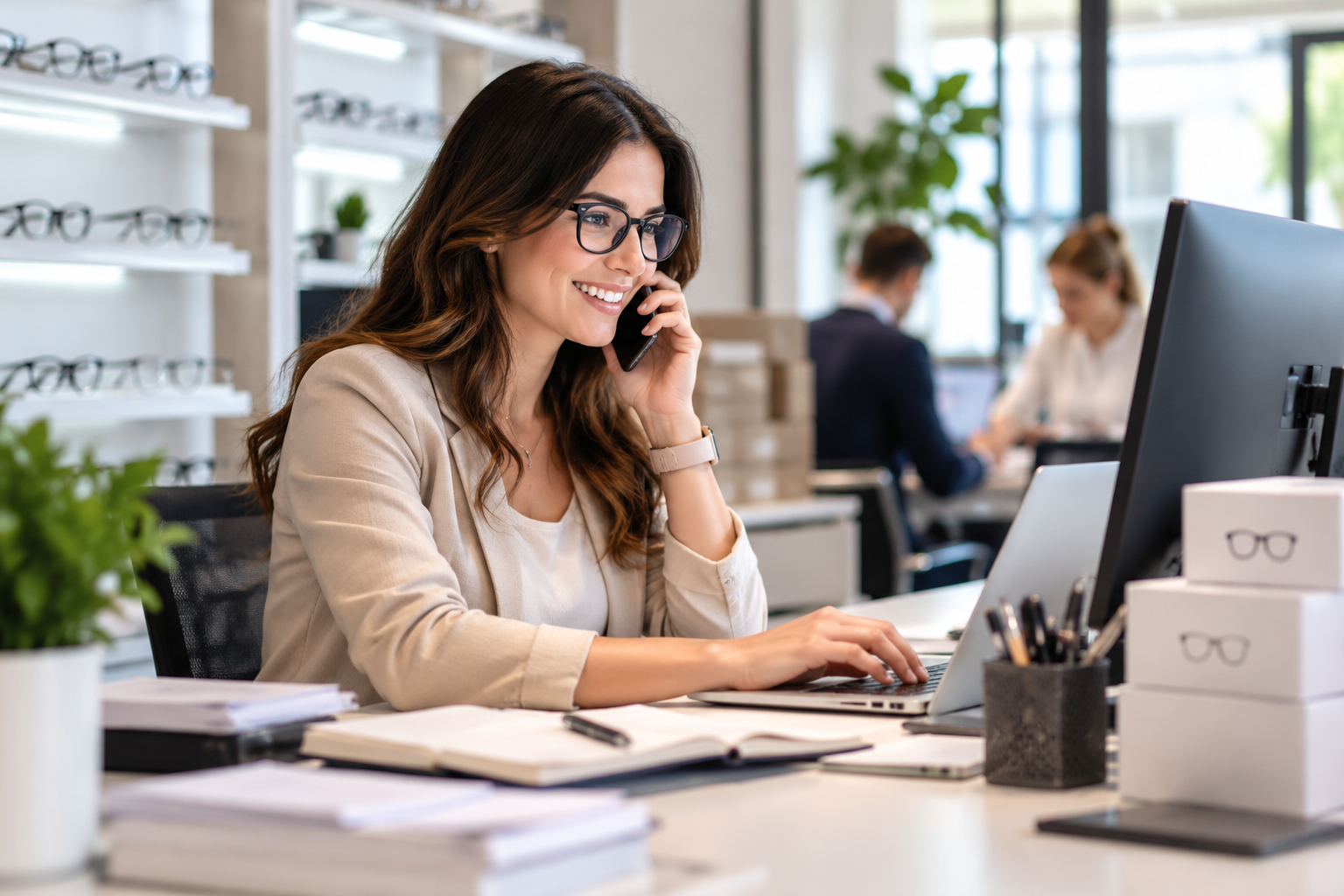 Una professionista al telefono e al computer in un negozio di ottica